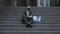 Sad young businessman in medical mask sitting on the stairs near office building. Feeling bad and annoyed. Unemployed