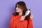 Sad young cute girl combing damaged hair, standing isolated on a pure background, looking away, combs tangled hair, wearing casual