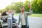 Sad young man standing on road next to broken car together with girlfriend, trying to call assistance. No connection