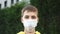 Sad young man teenager puts on a protective medical blue mask on a background of green vegetation. Bright yellow sweatshirt