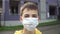 Sad young man teenager puts on a protective medical blue mask on a city street against the background of a blue residential buildi