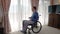 Sad young man in wheelchair looking through the window