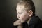 Sad young pre-school boy looking down and thinking. Unhappy child with sad face on dark background