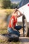 Sad young woman changing flat car tire with the spare one in field