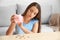 Sad young woman with empty piggy bank at home