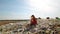 Sad young woman in red dress sits at huge trash dump with many seagulls in background