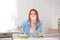 Sad young woman with taped mouth and burgers at table in kitchen.