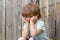 Sadness. Sad boy. A lonely child sits near a wooden fence. Frustration. Sad emotions. Experiences. Child psychology