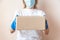 Safe contactless delivery service during quarantine. Young woman courier or volunteer holds cardboard box in medical gloves and
