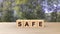Safe word wooden cubes on table vertical over blur background with climbing green leaves, mock up, template, banner with copy