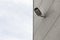 Safety cctv camera on gray tiled building facade, sky on other half of photo, diagonal view.