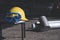 Safety goggles with yellow helmet and clipboard on metal chair with blurred aluminum round bars on the floor in workshop area