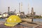 Safety Helmets and Book on Table Over Blurred Oil refinery background