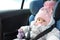 Safety seat for baby in car. Little cute girl in a pink hat and overalls sits winter in a child fastened with straps.
