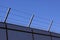 Safety wall with barbed wire and spikes on top of a fence provide security - blue sky background