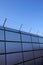 Safety wall with barbed wire and spikes on top of a fence provide security - blue sky background