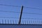 Safety wall with barbed wire and spikes on top of a fence provide security - blue sky background