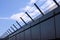 Safety wall with barbed wire and spikes on top of a fence provide security - blue sky background