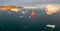 Sail boat with red sails cruising among ice bergs during sunset. Disko Bay, Greenland. Climate change and global warming