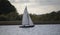 Sailboat cutting through the tranquil waters of a river with lush trees in the background