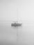 Sailboat on flat calm water with furled sails in eerie quiet morning fog