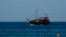 Sailboat floats by wavy sea surface far away under blue sky