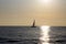 Sailboat on the horizon backlit with the ray of sun setting over the sea