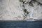 A sailboat motoring along on the sea under white cliffs close to the shore