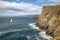 sailboat rounding the point, with dramatic cliff and ocean in the background