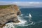 sailboat rounding the point, with dramatic cliff and ocean in the background