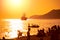 Sailboat in the sea in the evening sunlight and silhouettes of peoples on beach against beautiful sunny day before sunset