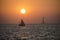A sailboat in the sea during sunset with a lighthouse in the background