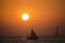 A sailboat in the sea during sunset with a lighthouse in the background