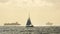 Sailboat silhouette sails on shining water of ocean , big cargo ships in background