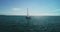 Sailboat with white sails sailing in the sea toward horizon with sun rays, aerial view in 4k video