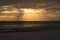 Sailboats on the horizon as the sun peeks through clouds with beams of light during sunset on Fort Myers Beach