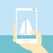 Sailing boat mobile photo with human hand, blue sea and sky.