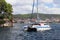 Sailing catamaran sails along the rocky green coast past the red literary sign - the fairway lighthouse. City of Sibenik in the Da