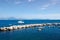 A sailing catamaran yacht lies moored just outside a stone wave breaker in the Bay of Naples, with the Amalfi Coastline in the bac