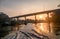 Sailing long-tail boat with sunrise on bridge in river kwai