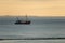 Sailing ship at sunrise in a calm sea with windmills on the horizon in Norderney, Germany