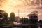 A sailing traditional dutch boat anchored in a canal outside a house with golden cloudy sky, Holland.