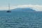 A sailing yacht in the sea in the morning sunlight against the beautiful mountains shrouded in clouds