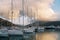 Sailing yachts stand on the pier near the mountain range against the backdrop of sunset pink clouds