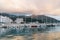 Sailing yachts stand in a row on the pier with colorful villas at the foot of the mountains in the reflections of sunset