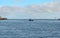 Sailors working on a boat in the water with the horizon line in the background on a cloudy day with blue sky and lighthouses