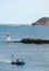 Sailors working on a boat in the water with the horizon line in the background on a cloudy day with blue sky and lighthouses