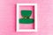 Saint Patrick leprechaun paper hat in photo frame on pink glitter background.