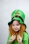 Saint Patricks Day. Endearing smiling small girl with decorative red beard, green shamrok leaf on her cheek and leprechaun hat,