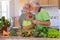 Saint Valentine`s day. Elderly man offers a rose to her wife while kissing her. Beautiful senior couple in home kitchen while